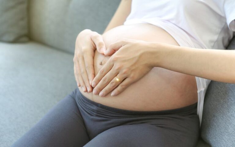 A young mother is making a heart-shaped hand on her stomach